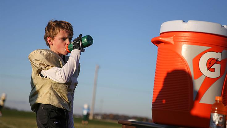 Youth football player taking a drink break on the sideline next to a Gatorade cooler